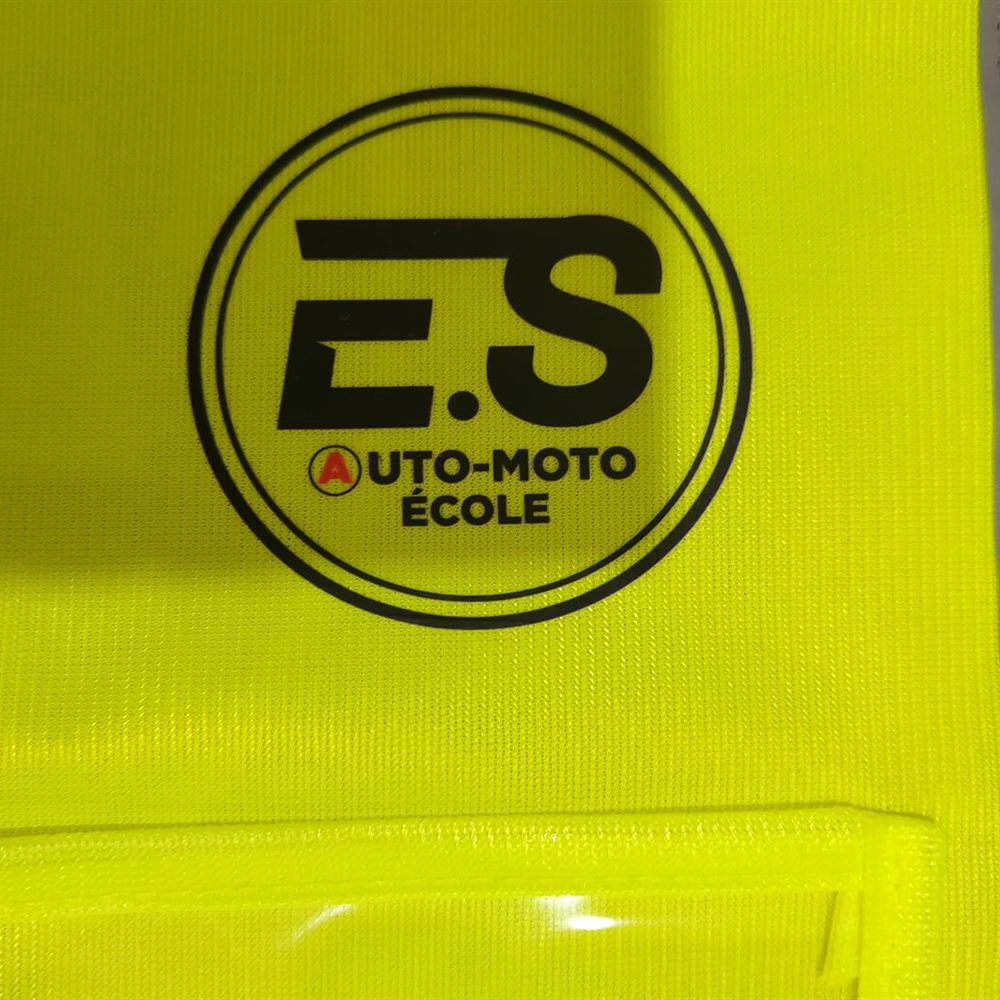 Gros plan du logo d'auto-école floqué sur un gilet réfléchissant jaune
